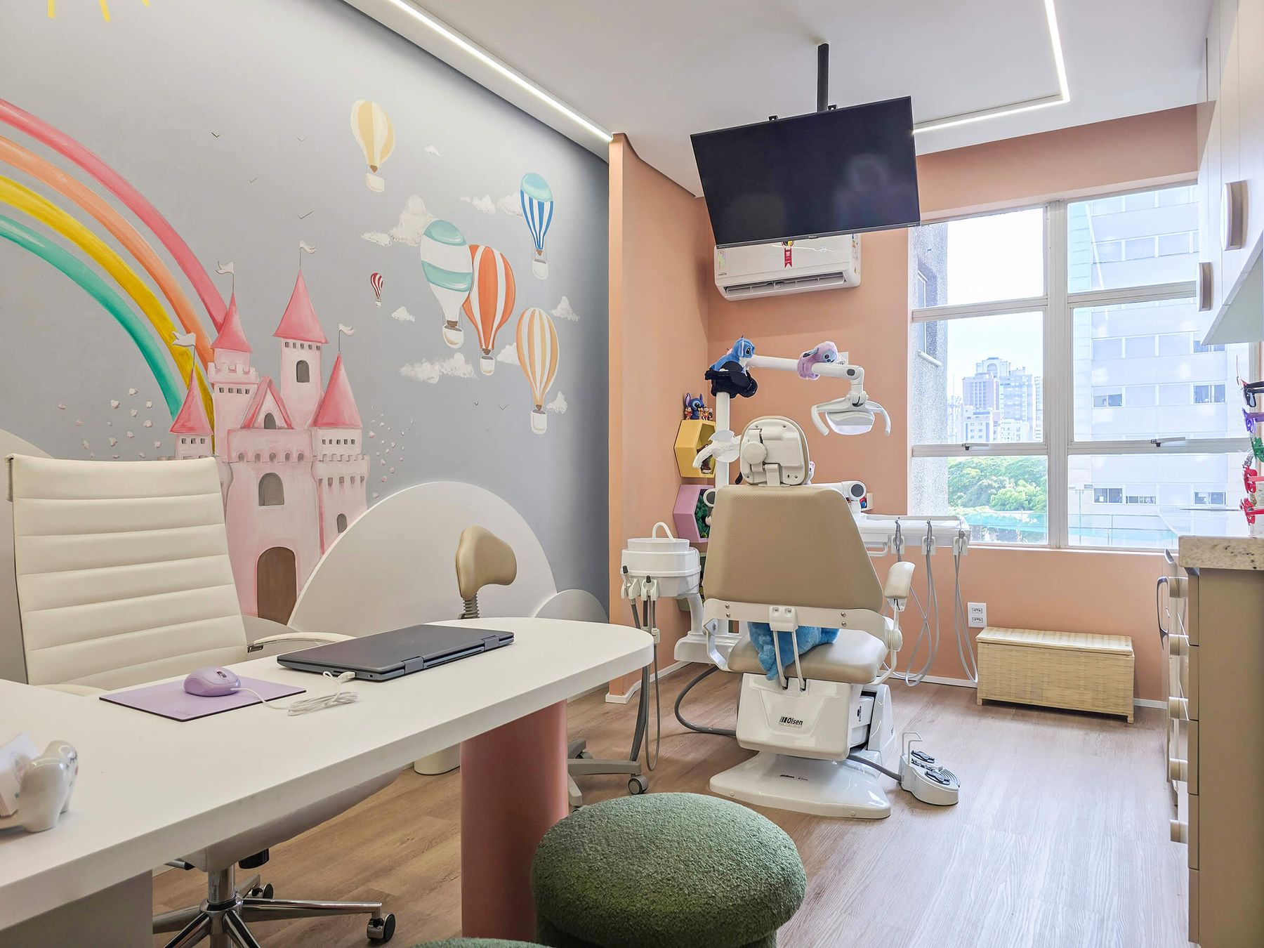 A sala de atendimento do Mundo Encantado, com o mural do castelo rosa e do arco-íris, a cadeira e a janela